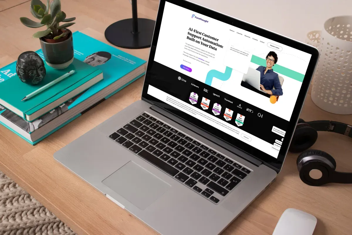 Laptop on a wooden desk showing the Forethought.ai homepage, headlined AI-First Customer Support Automation.