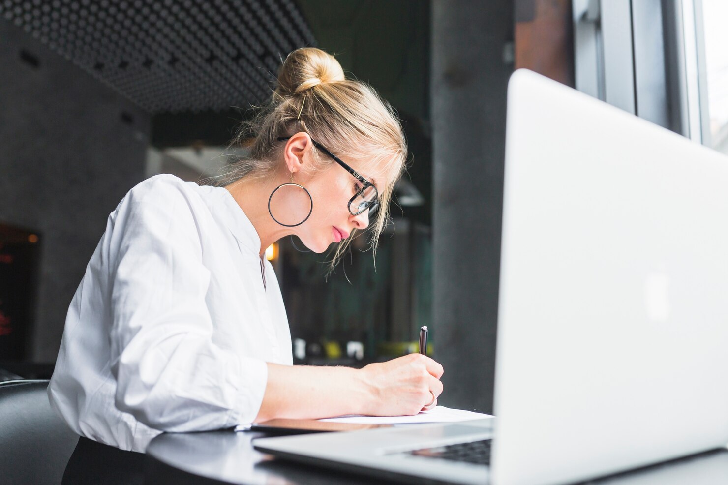 Woman writing on document with laptop on desk. She is creating a WordPress disaster recovery plan