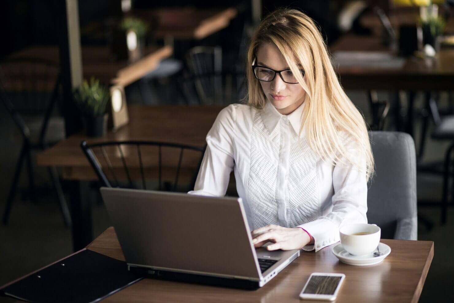 Business woman working on summarising the role of Unlimited WordPress Support in handling Site Load and Traffic Spikes on her laptop in a cafe, drinking coffee