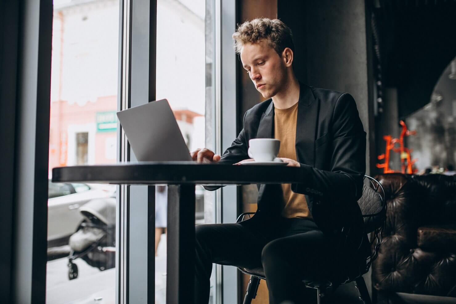 Handsome man working on a computer in a cafe and drinking coffee. He is creating a list of the various types of payment gateways for WooCommerce