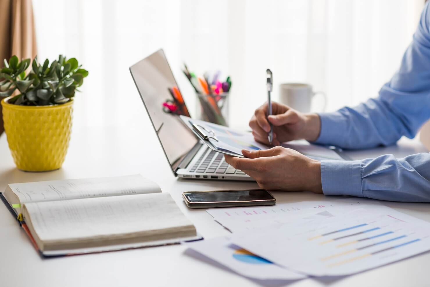 Man writing in documents in office based on automated website audit. He is trying to put the dots together himeslef regarding the challenges his website is experiencing