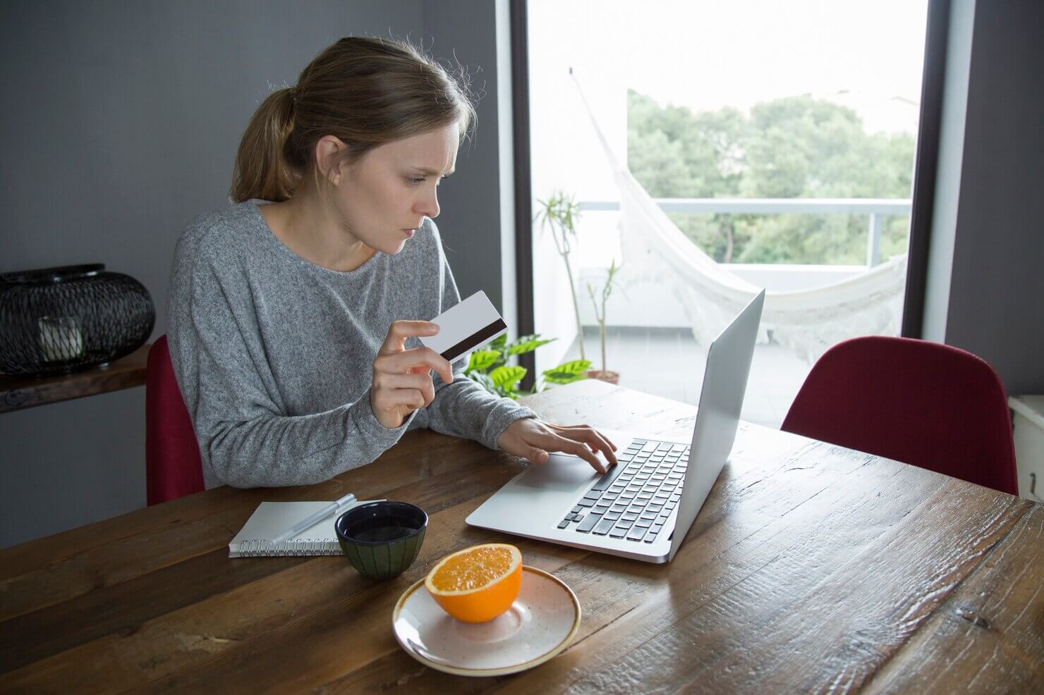 Young woman making online shopping with credit card on PC in her kitchen at the table