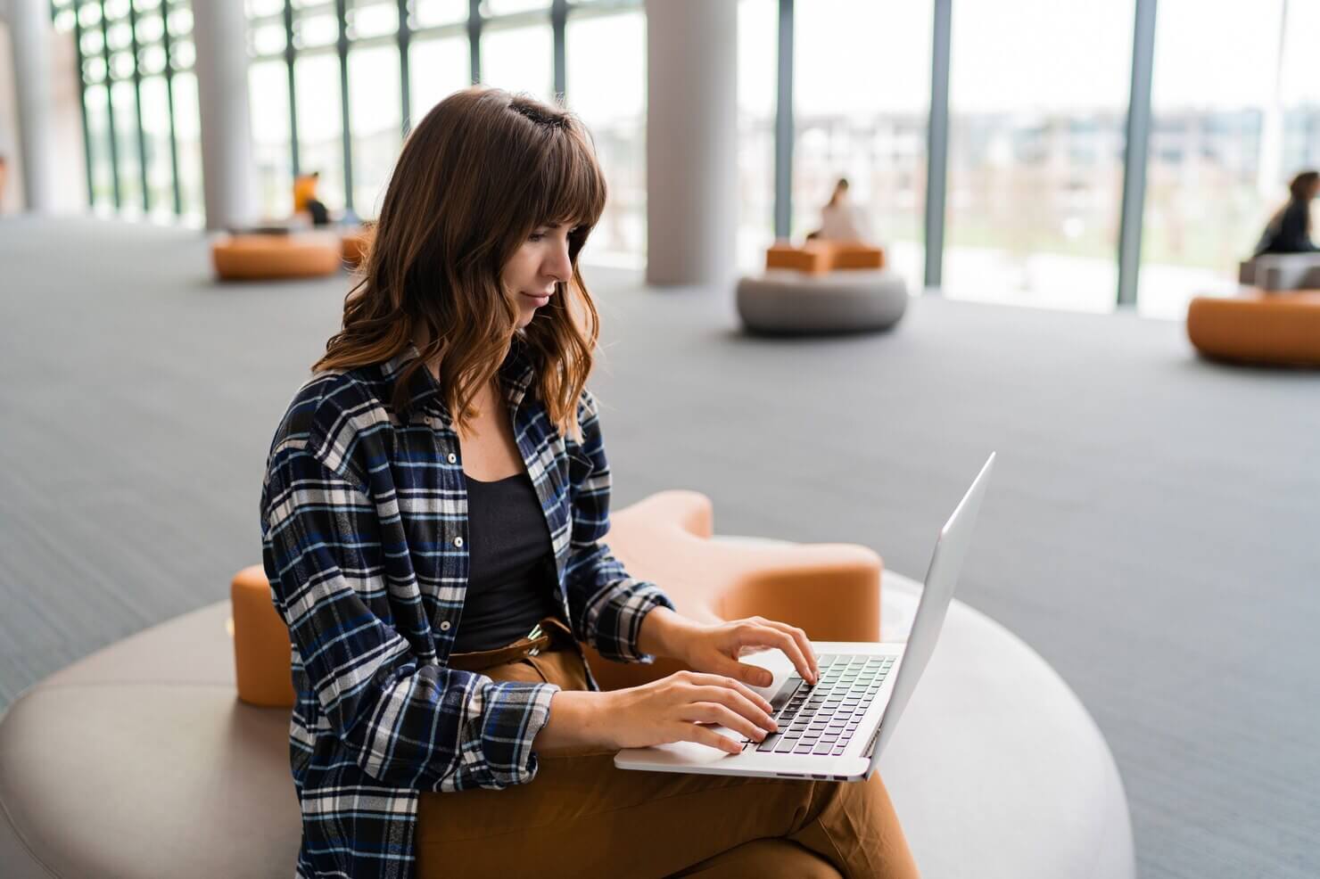 Happy woman using lap top while sitting at airport lounge. She is working remotely, rewriting content on her website